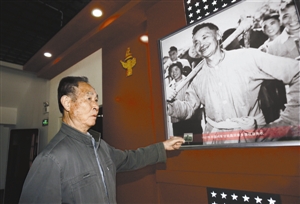 在甘祖昌展览馆，周晓平手持照片小样，给记者讲述甘祖昌当年带领乡亲们劳动的情景。