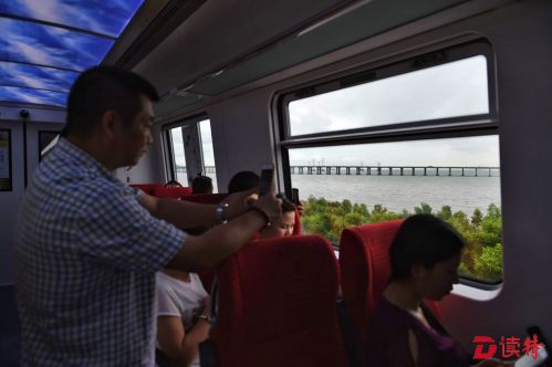 列车经过海边，乘客拿出手机拍摄。