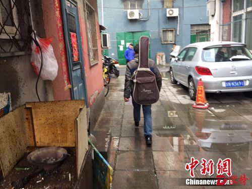 图为樊富贵背着吉他走出医院旁边租来的住所。吕春荣 摄