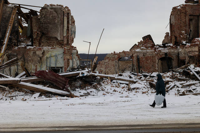 当地时间2023年2月13日，乌克兰哈尔科夫地区，一位老妇人走过一栋因炮击而被毁的建筑。