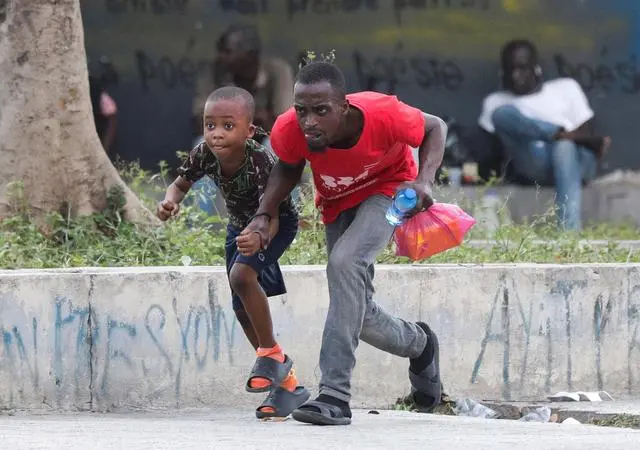 2024年3月21日，在海地首都太子港街头，人们俯身奔跑躲避流弹。新华社/路透